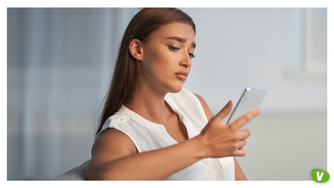 Sad girl holding cellphone sitting on sofa at home