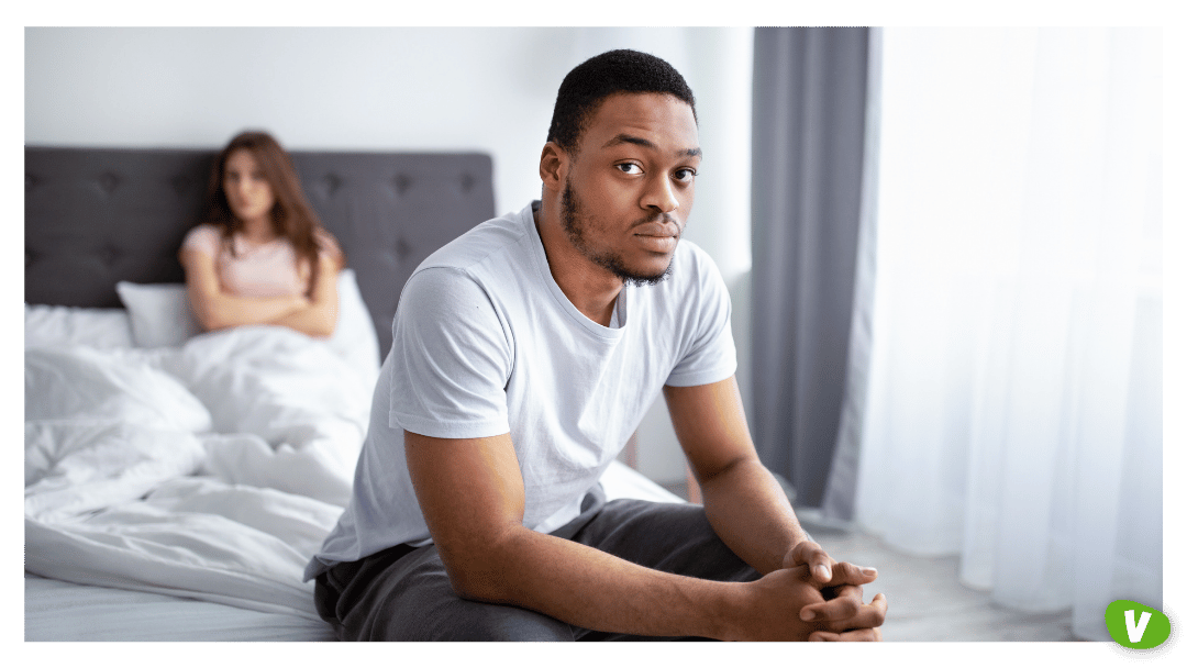 Erectile dysfunction, or relationship problems. Upset black guy sitting on bed, his dissatisfied wife on background